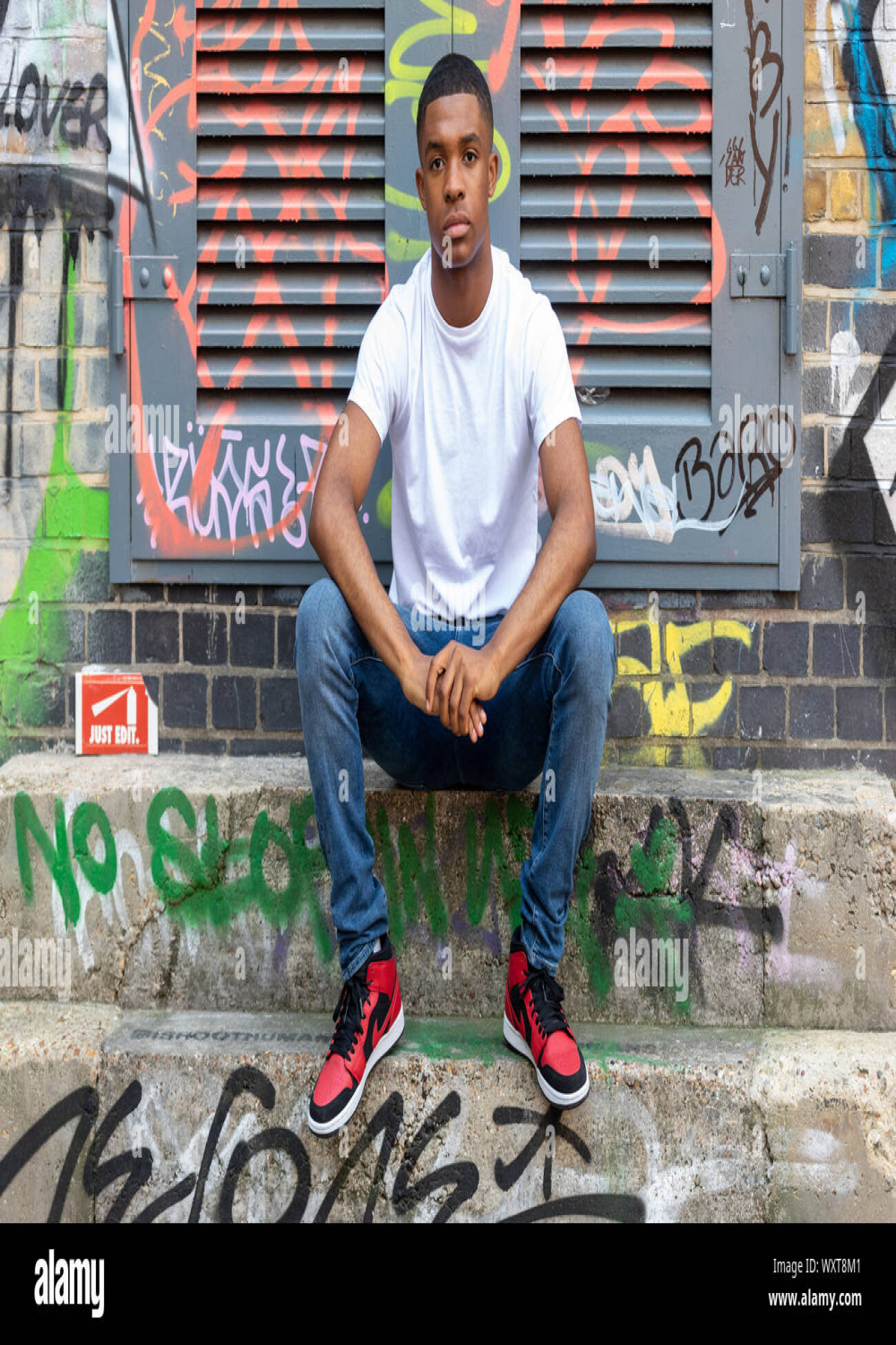 A young man poses on some steps with a grafitti wall in the